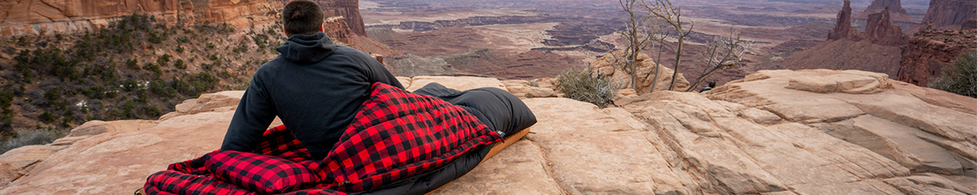 A man sits inside his TETON Sports Celsius XXL Sleeping Bag while viewing a valley below.