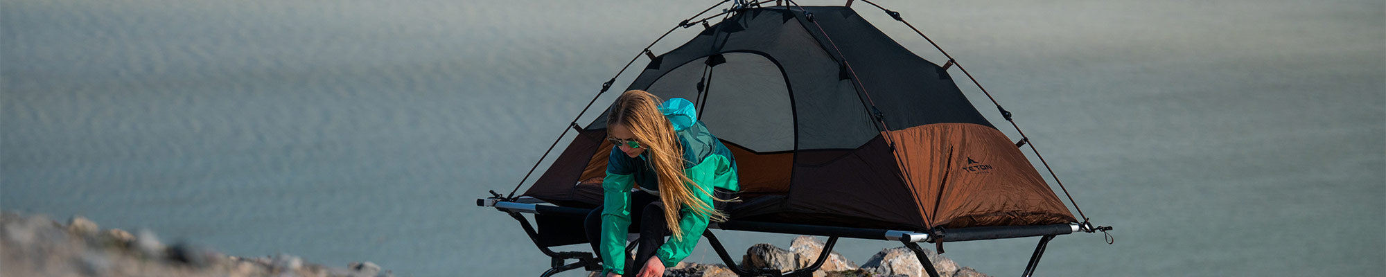 A woman puts on her shoes while leaving her TETON Sports Vista Tent Bundle.