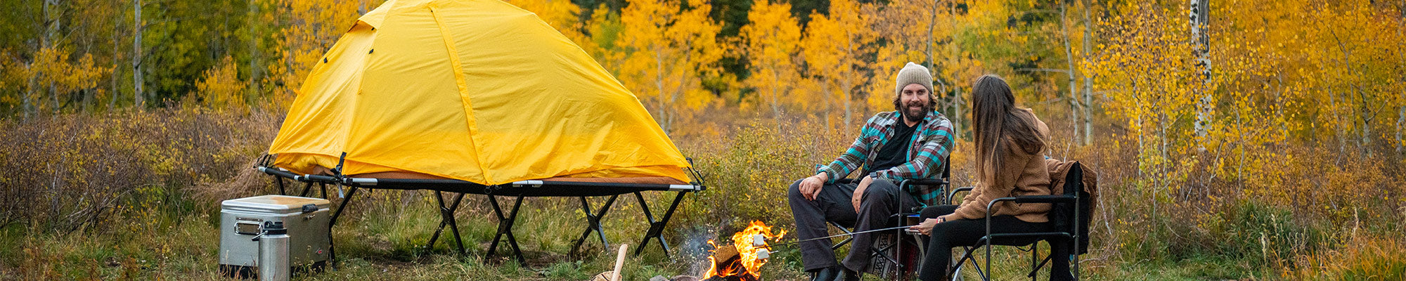 A couple camps togther in a beautiful autumn forest with their TETON Sports Vista Tent Bundle.